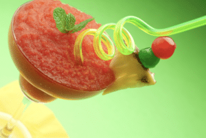 frozen strawberry daiquiri in glass trimmed with mint, pineapple garnish and neon green swirly straw